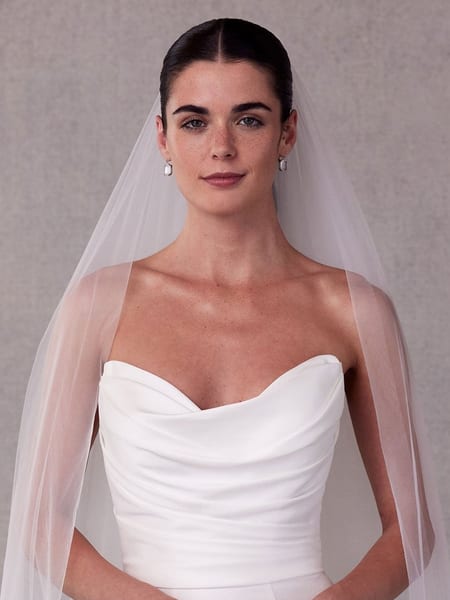 Model wearing a sheer fingertip-length tulle veil over her shoulders with a strapless gown